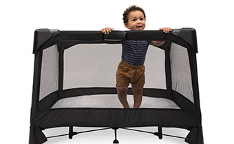 A toddler standing in a portable crib